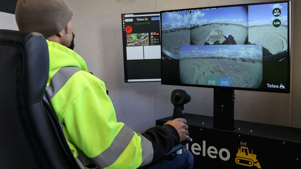 An operator controls two John Deere 333G compact track loaders, switching between remote operation and autonomy.